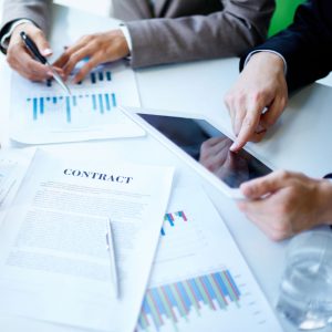Photo of business documents, and a tablet computer being used in a business meeting.